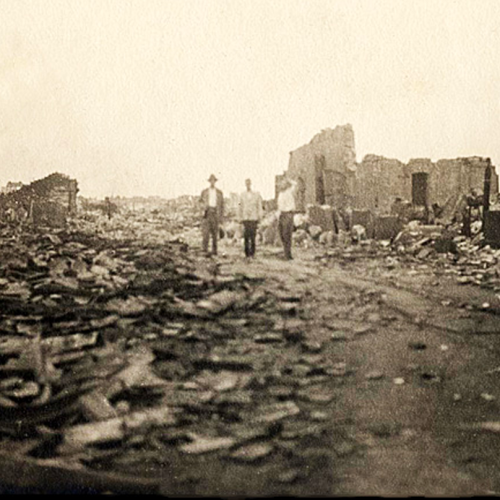 three people standing in the ruins of a city hit by an earthquake